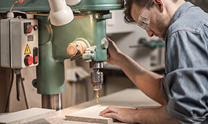 Photo of joiner in protective glasses drilling wooden board