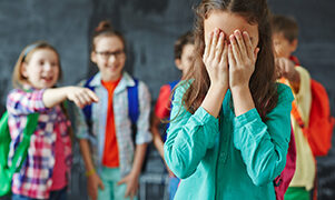 Schoolgirl crying on background of classmates teasing her